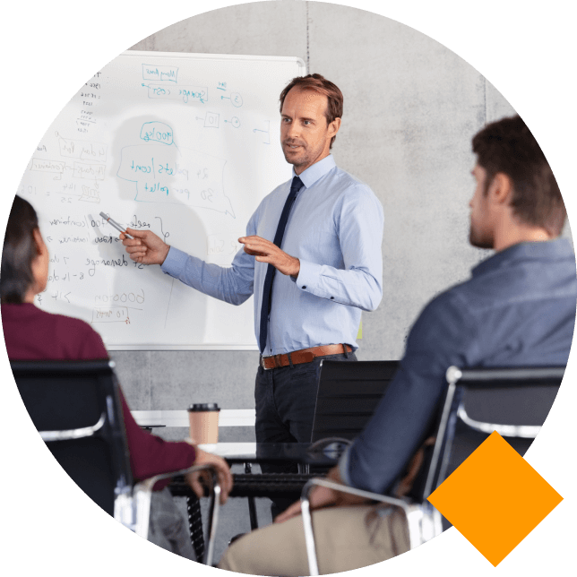 Professional instructor standing at whiteboard explaining something to two seated professionals