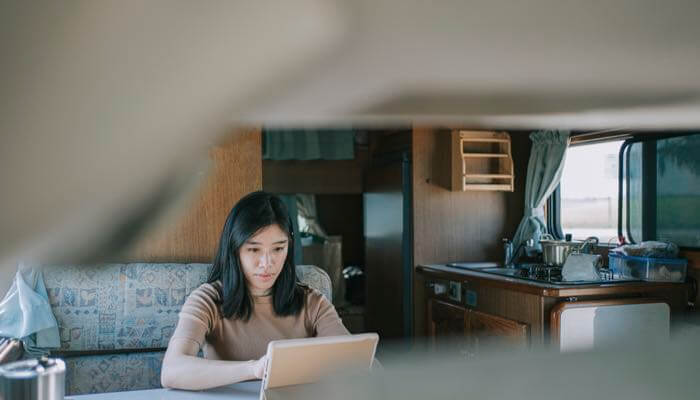 Young diverse female sitting at her kitchen table & working on her laptop