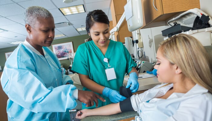 Two female health care professionals preparing to administer a blood test on a female patient