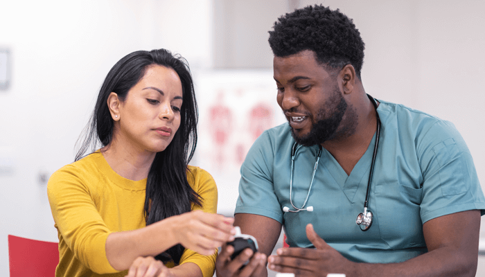 Diverse male health care professional showing diverse female patient a glucose monitor
