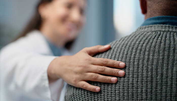 Female health care professional smiling with hand on male patient's shoulder